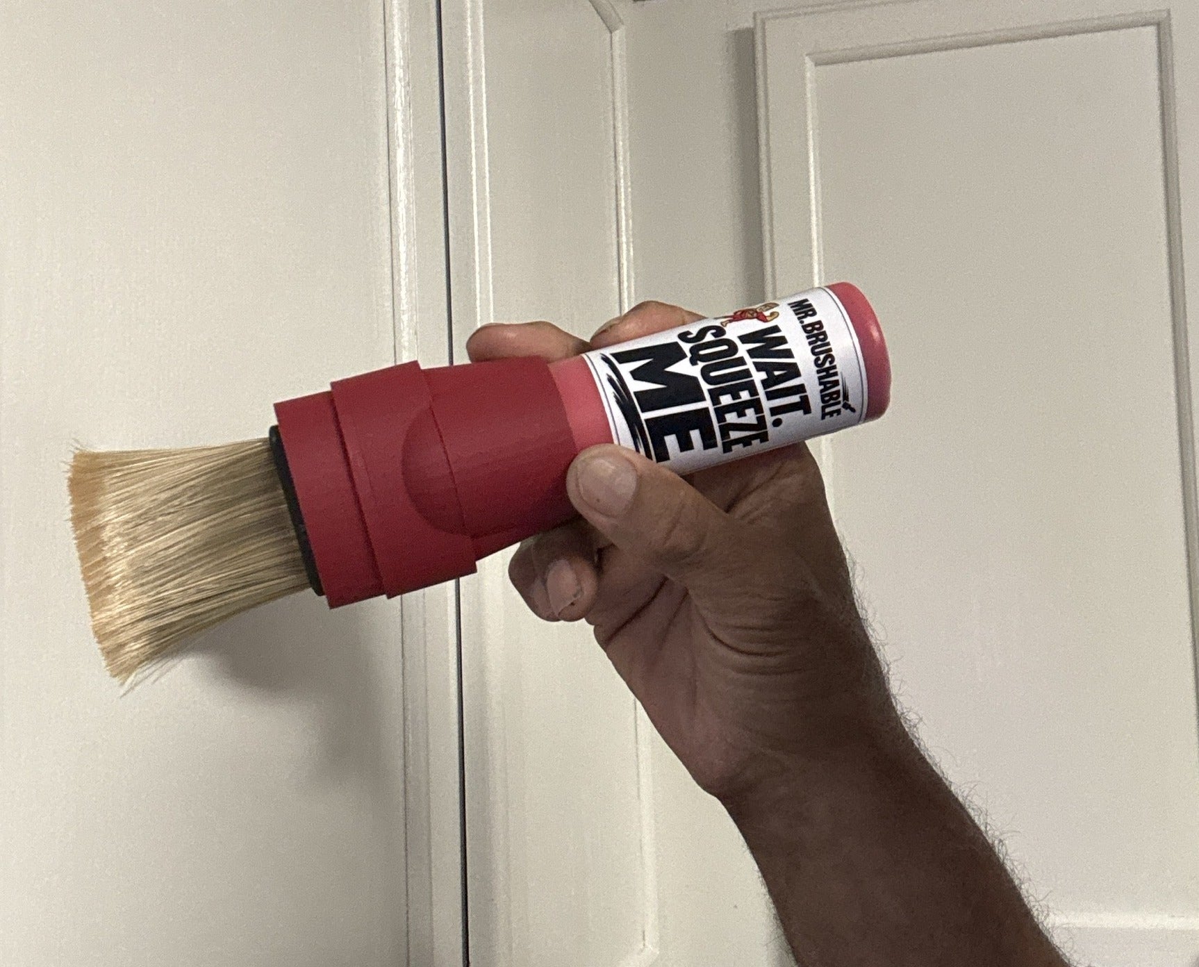 A red Mr. Brushable brush bottle touching up the edge of a white door